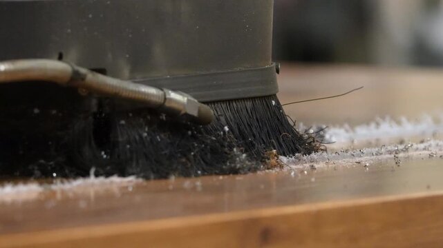 Macro shot of a CNC router bit and brush attachment carving a precise groove into a wooden plank, scattering shavings in a professional woodworking factory.