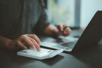 Person Using Calculator and Laptop for Financial Work in Office Setting
