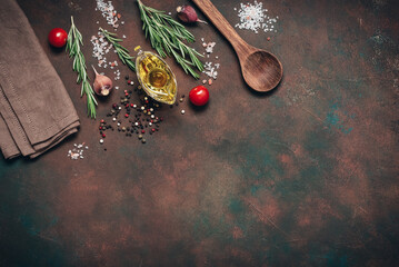 Spices, herbs, olive oil, and a wooden spoon on a dark rustic background. Culinary backdrop, corner frame, top view, flat lay.