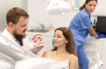 Obraz premium Male dentist shows a jaw model to a young patient in a dental clinic