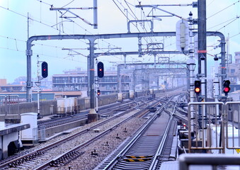 曇り空の下に広がる複雑な鉄道の線路と赤信号。日本の都市部における交通インフラの風景