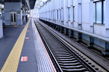 Naklejka premium 駅のホームと線路、安全を支える黄色の点字ブロックが続く風景（公共交通機関・バリアフリー）