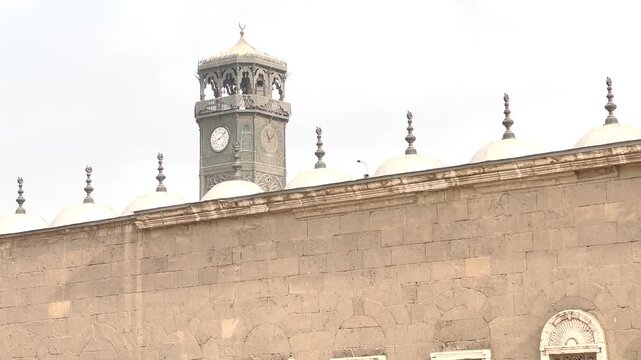 View of a historic stone wall and clock tower in Cairo, Egypt. Exterior architectural detail with traditional design elements and urban background, suitable for themes of heritage, architecture.