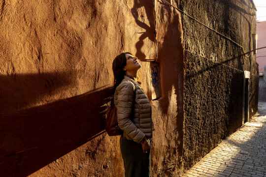 At Medina, a woman looks up at a shadow on a textured wall in a narrow alleyway, bathed in golden light. Jamaa el Fna,Marrakech,Unesco hertage,Morocco