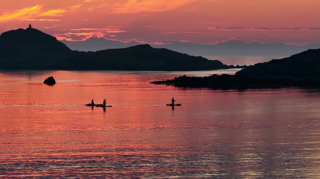 drone flight above sea at Ramberg beach, midnight sun in summer. 3 people on SUP board stand-up paddleboard enjoying sea and midnight sun in arctic Norway. Amazing nature, travel destination.