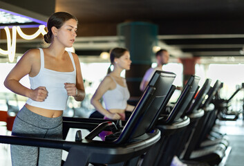Fototapeta premium Young athletic woman training by running on treadmill in gym