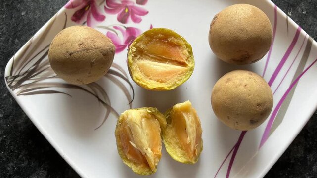 Fresh whole and sliced sapodilla fruit (Chiku) showing pulpy texture on a floral plate