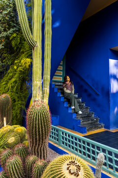 A woman sits on blue stairs near cacti, looking up. Jardin Majorelle,Marrakech,Morocco