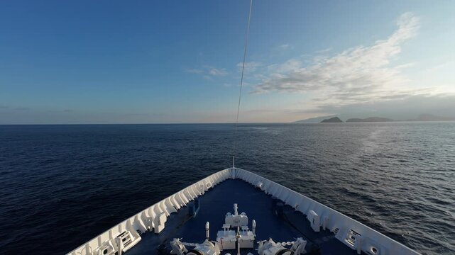 Forward deck of ship heading into open sea with distant islands