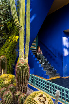 A woman sits on blue stairs surrounded by cacti. Jardin Majorelle,Marrakech,Morocco