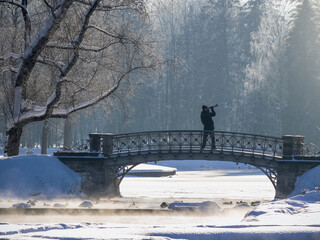 A man is taking a picture of a bridge over a frozen river