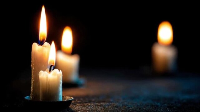 Three lit candles stand against a dark backdrop their flames flickering and casting a warm glow