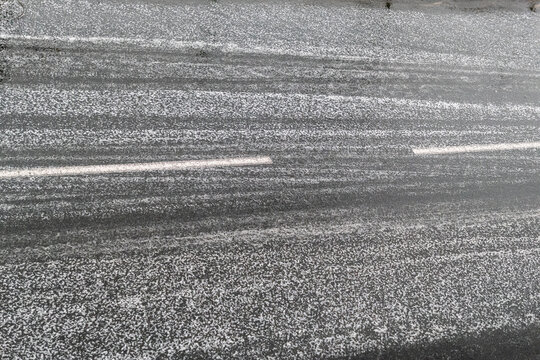 Estrada de asfalto coberta por uma camada densa de granizo e gelo sob condi&ccedil;&otilde;es meteorol&oacute;gicas adversas de inverno causando perigos adversos para os condutores