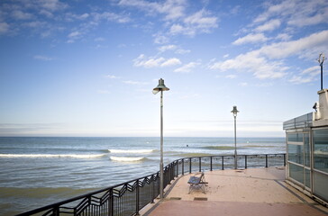Passeggiata sul lungomare con panchine, lampioni e vista infinita, sotto un cielo sereno con leggere nuvole