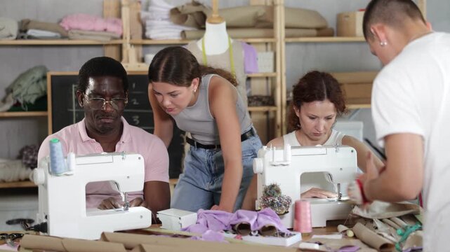 In beginner sewing class attended by people of different ages and backgrounds, experienced tailor showing student how to properly thread machine before stitching during practical work