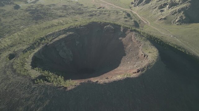Aerial view of Khorgo extinct volcano crater in Mongolia, drone flying into ancient caldera, young green coniferous forest and black lava rocks, 4k raw unedited footage