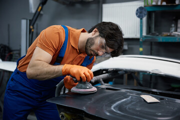Auto worker technician is sanding and polishing a car inside a garage workshop environment