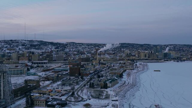 Wide aerial view of Duluth city and the frozen shoreline of Lake Superior during winter dusk.