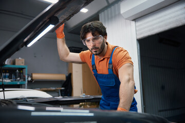 Auto mechanic inspecting car engine under the hood in garage