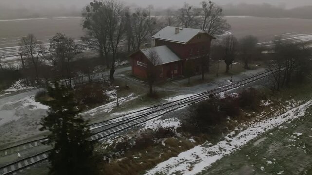 Aerial reveals old Rural brick railway station on single track line with passing loop in winter. Remote countryside scene suitable for travel, documentary, and vintagel use.