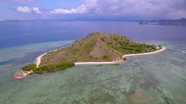 Backward-moving aerial footage revealing Kanawa Island, a small tropical island surrounded by crystal-clear turquoise waters and coral reefs in Komodo National Park, Indonesia.