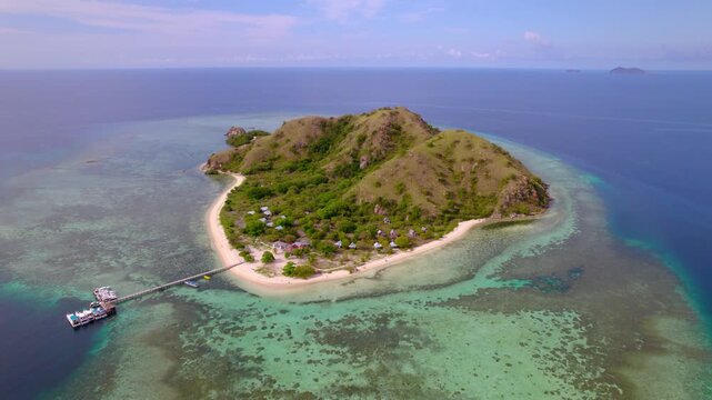 Approaching aerial revealing Kanawa Island, a small tropical island surrounded by crystal-clear turquoise waters and coral reefs in Komodo National Park, Indonesia.