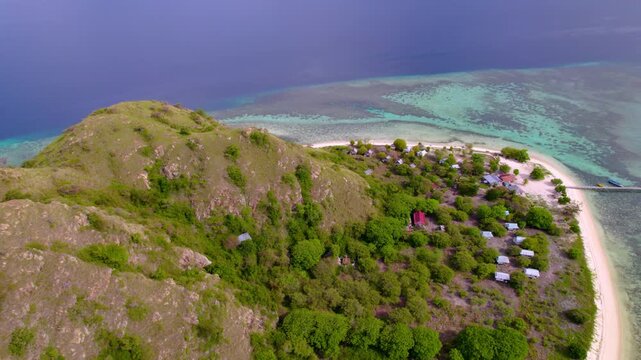 Backward aerial showing beachfront cottages and white sand beaches engulfing the turquoise waters of Kanawa Island in Indonesia.