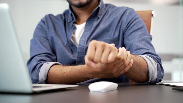 Close up. Businessman holding wrist in pain while using computer mouse. A man massages painful hand does an exercises Concept of ergonomic challenges or strain injury in professional work environment