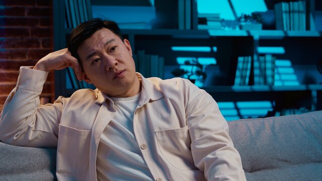 Upset Asian middle-aged man choosing tv channel boring cinema at night evening insomnia at home relaxed Korean Chinese Japanese male choose searching television program search movie feeling boredom