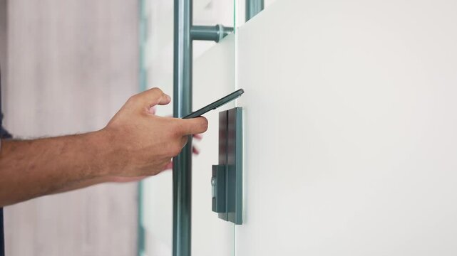 Close up of businessman hand unlocking glass door using mobile phone application and enters modern office. Scanning open smartphone with mock up screen app. Smart electronic locks with keyless access