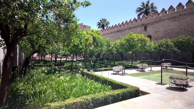 Wide POV shot walking toward the central stone fountain in the sunlit Patio de Crucero at the historic Alc&aacute;zar de los Reyes Cristianos in Cordoba, Spain.