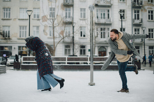 Loving couple having playful snowball fight in winter city