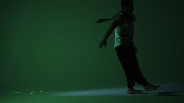 A man wearing loose, baggy pants performs a smooth backward roll, illuminated by dynamic green stage lighting. Video captures the fluid motion.