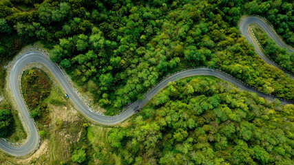 Aerial view with vehicle driving on highway road in green forest. Sustainable transportation, zero emissions, and eco-friendly