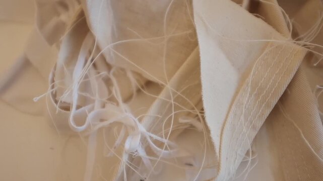 A high-angle, close-up tracking shot of a messy pile of unbleached cotton fabric scraps, frayed edges, and loose white threads. The video showcases the raw texture of textile manufacturing waste.