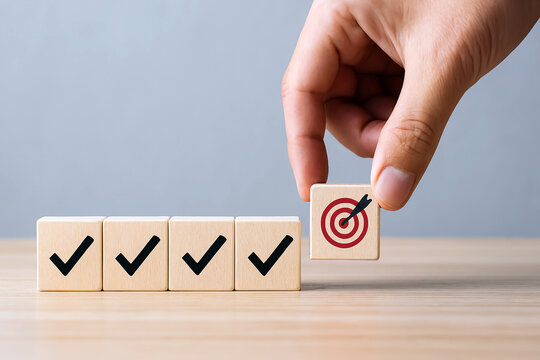Hand placing final wooden block with target icon onto four checked blocks. AI-powered completion certification, real-time milestone validation, sustainable success path, warm beige background.