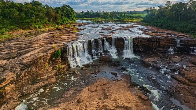 Aerial view of Sae Pong Lai Waterfall reveals a tropical river cascading over layered rock formations, surrounded by lush green forest and untouched wilderness.
