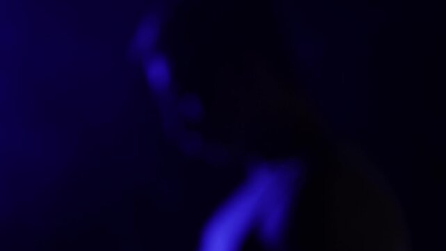 A charismatic muscular man with a mustache, captured in profile, flinches as a powerful spotlight hits his face, quickly raising his hand to block the light. Close-up.