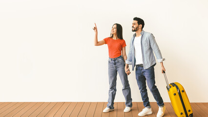 Hot tours. Loving couple with suitcase walking and holding hands, woman pointing at free space,...