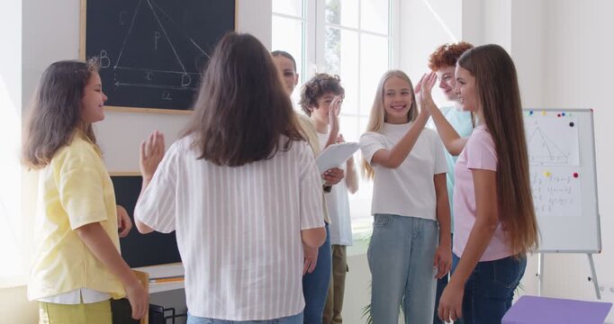 Teacher gives a high five to a group of students during a lesson in the school classroom. The children work together, displaying teamwork, and positive interaction in a happy learning environment.