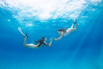 Two girls swim and explore vibrant marine life while snorkeling in the sea on a sunny day