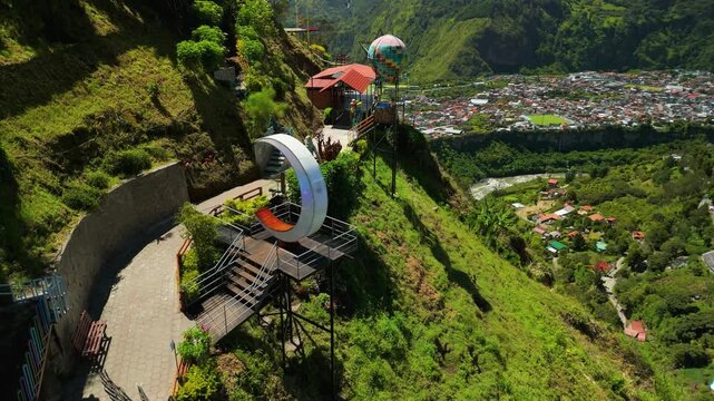 Drone flies toward the unique photo installations at Mirador Secreto del Abismo including Moon photo deck and hot air balloon overlooking a deep canyon in Banos Ecuador