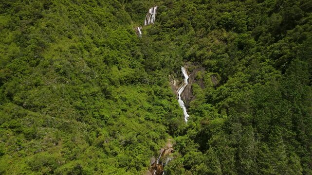 Cinematic drone shot follows rushing mountain river rapids through dense tropical forest to reveal majestic Cascadas Chamana waterfall in Ulba valley near Banos de Agua Santa Ecuador