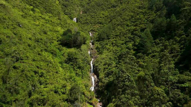 Drone rises and tilts up from rushing mountain river rapids to reveal the majestic Cascadas Chamana waterfall tucked inside a lush tropical gorge near Banos de Agua Santa Ecuador