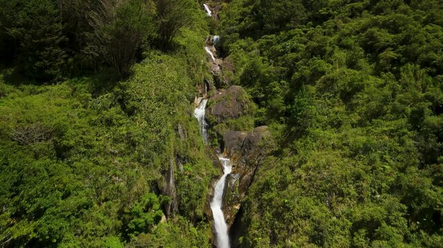 Drone flies over fast-moving mountain river rapids and white water at the base of the Cascadas Chamana waterfall surrounded by dense tropical rainforest in Banos de Agua Santa Ecuador