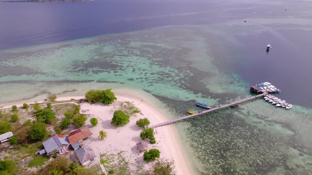 Backward aerial showing private yachts, beachfront cottages and white sand beaches of Kanawa Island in Indonesia.