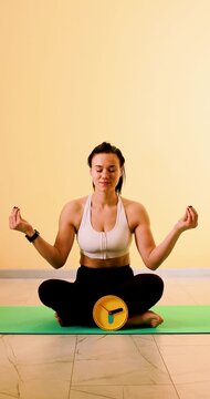 Vertical close-up of a girl meditating on a yoga mat with a yellow clock beside her. Concept of mindfulness, wellness, time management, and healthy lifestyle. 4K vertical video.