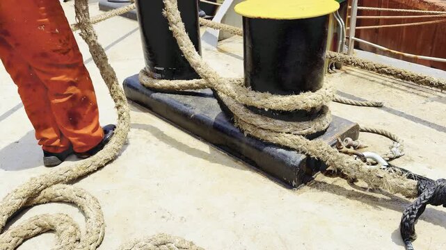 merchant navy deckhand or sailor secure the vessel using a thick mooring rope around a sturdy double bollard. strict maritime safety protocols crew members