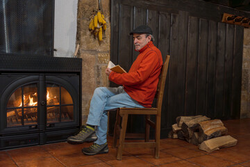 Senior man reading book by warm fireplace
