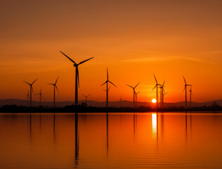 Obraz premium Sunset Silhouette of Wind Turbines Reflected in Calm Lake, Celebrating Renewable Energy Harmony and Tranquil Evening Serenity